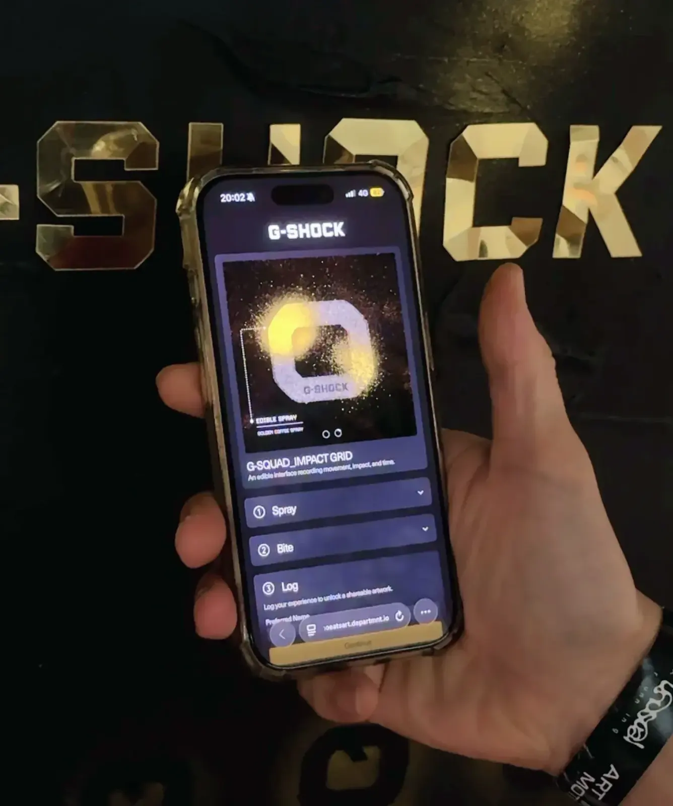 A guest holding a phone open on the G-SHOCK Portal in front of the G-SHOCK wall, an event wristband on their wrist