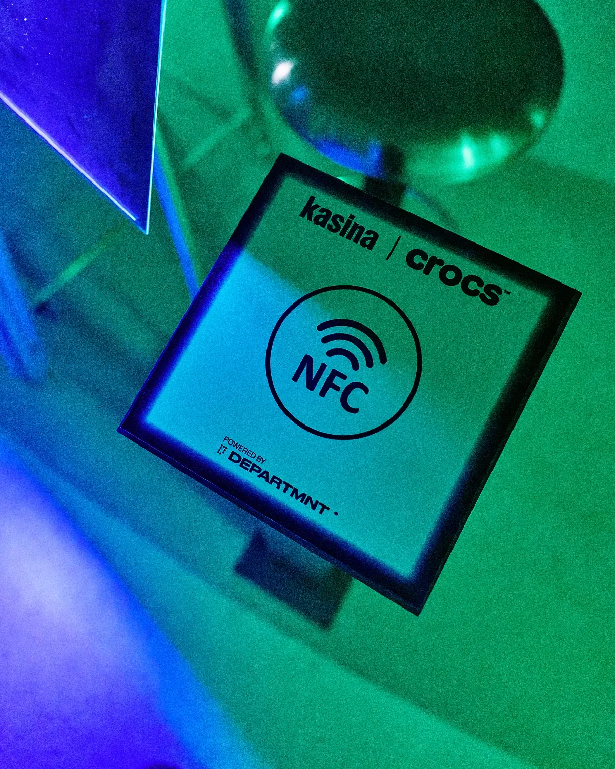 A Kasina × Crocs NFC touchpoint plate in the store, lit green and blue